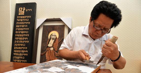충북 음성군 대소면 대동로 한 공방에서 서각 예술가 엄재봉씨가 망치와 칼로 목판 위에 그림을 그리고 있다.  사진=음성군 제공
