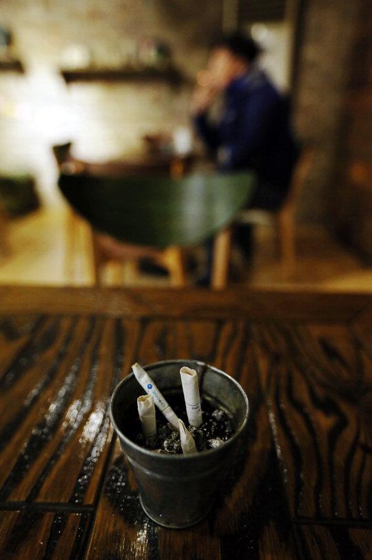 한 커피숍 내 흡연실에서 한 남성이 담배를 피우고 있다. 올해 강화된 금연법에 따르면 흡연실 설치 시 의자나 탁자 등 편의 시설을 설치할 수 없고, 음료 반입도 금지되지만 이를 지키는 영업소는 많지 않은 실정이다. [연합뉴스]