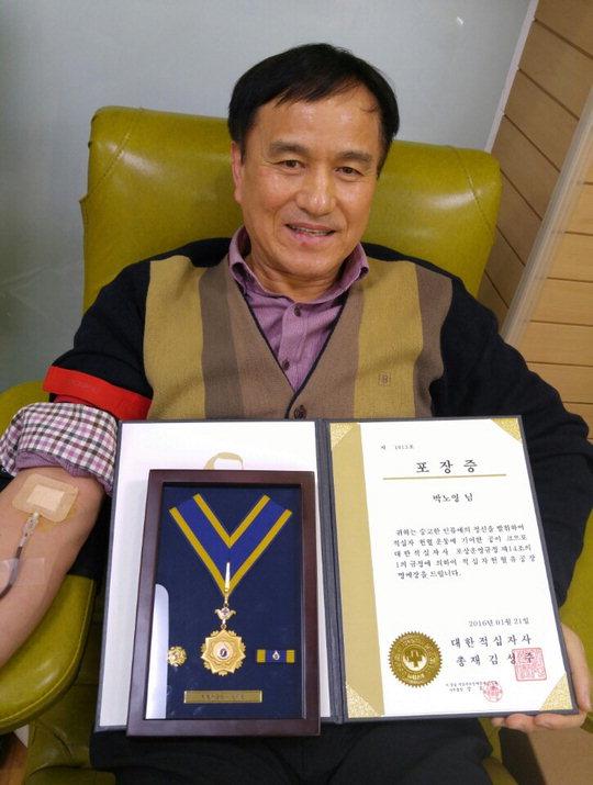  100번째 헌혈을 통해 적십자 헌혈 레드카펫인 '헌혈 명예의 전당'에 이름을 올린 청주교도소 박노영(58)교도관이 '헌혈유공장 명예장'을 들어 보이고 있다. 사진=공주대학교 헌혈센터 제공