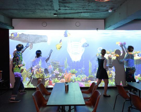 지난 19일 서울 송파구에 오픈한 뉴딘플렉스의 스크린낚시 브랜드 `피싱조이` 첫 직영점에서 이용객들이 매장 한 편에 설치된 체험형 스크린에서 바다속 물고기를 만지고 있다. 사진=뉴딘플렉스 제공
