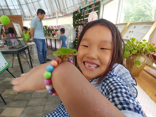 개구리 특별전시장을 찾은 한 어린이가 실물 개구리를 손등에 올려놓고 신기 한듯 바라보며 환하게 웃고 있다. 사진=늘푸른나무 제공
