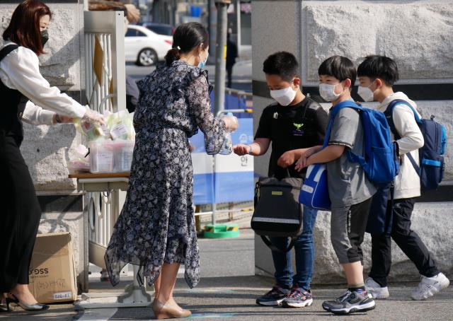 대전의 한 초등학교 교문 앞에서 학생들이 발열검사와 손 소독을 하고 교사의 안내를 받고 있다 [사진=대전일보DB]